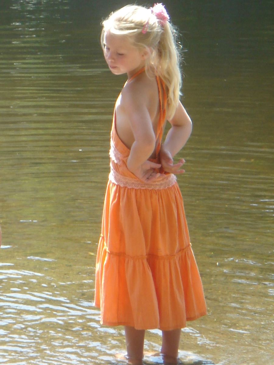 Eva als jong meisje in een oranje jurk, tot haar enkels in het water